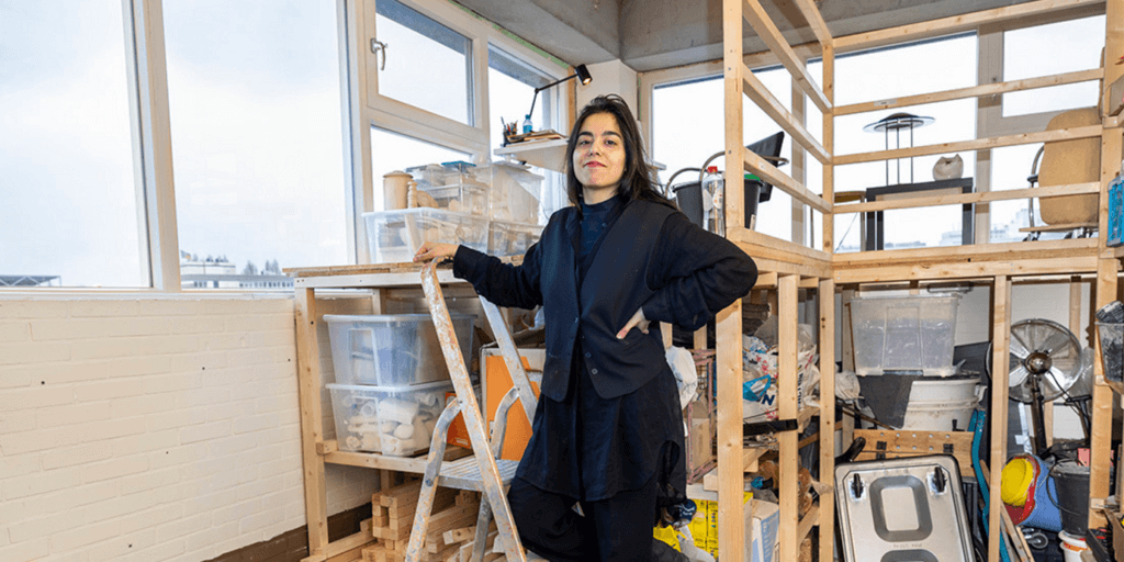 Kunstenares Narges staat op een ladder in haar atelier. Ze kijkt trots de camera in.