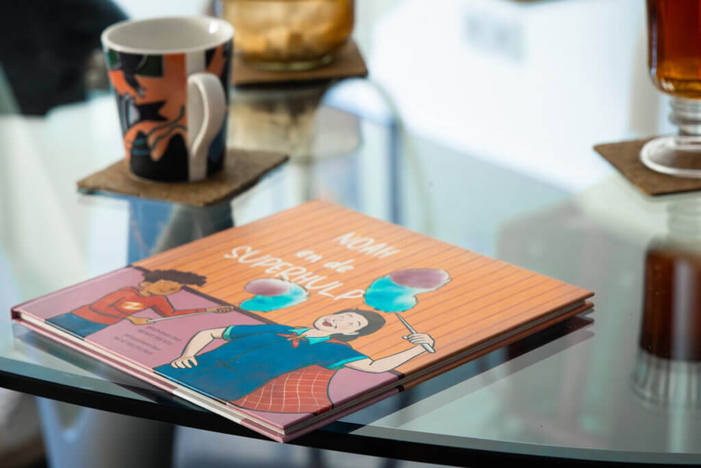 Op een glazen salontafel ligt het voorleesboekje 'Noah en de superhulp' naast een kopje koffie. 